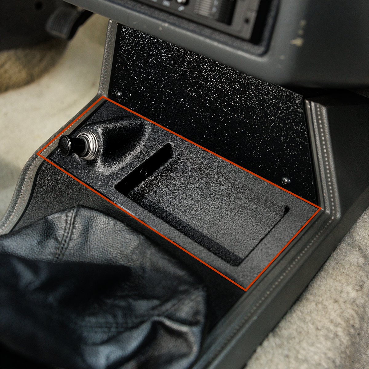 Car console with a black tray and orange trim on a gray carpeted floor.
