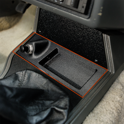 Car console with a black tray and orange trim on a gray carpeted floor.